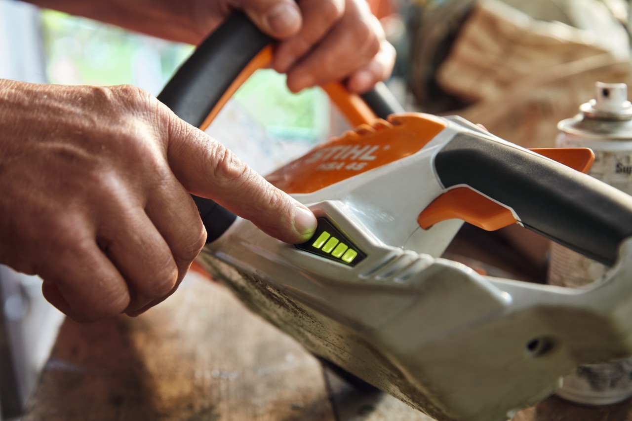 O persoană verifică nivelul de încărcare al trimmerului de gard viu fără fir STIHL HSA 45.