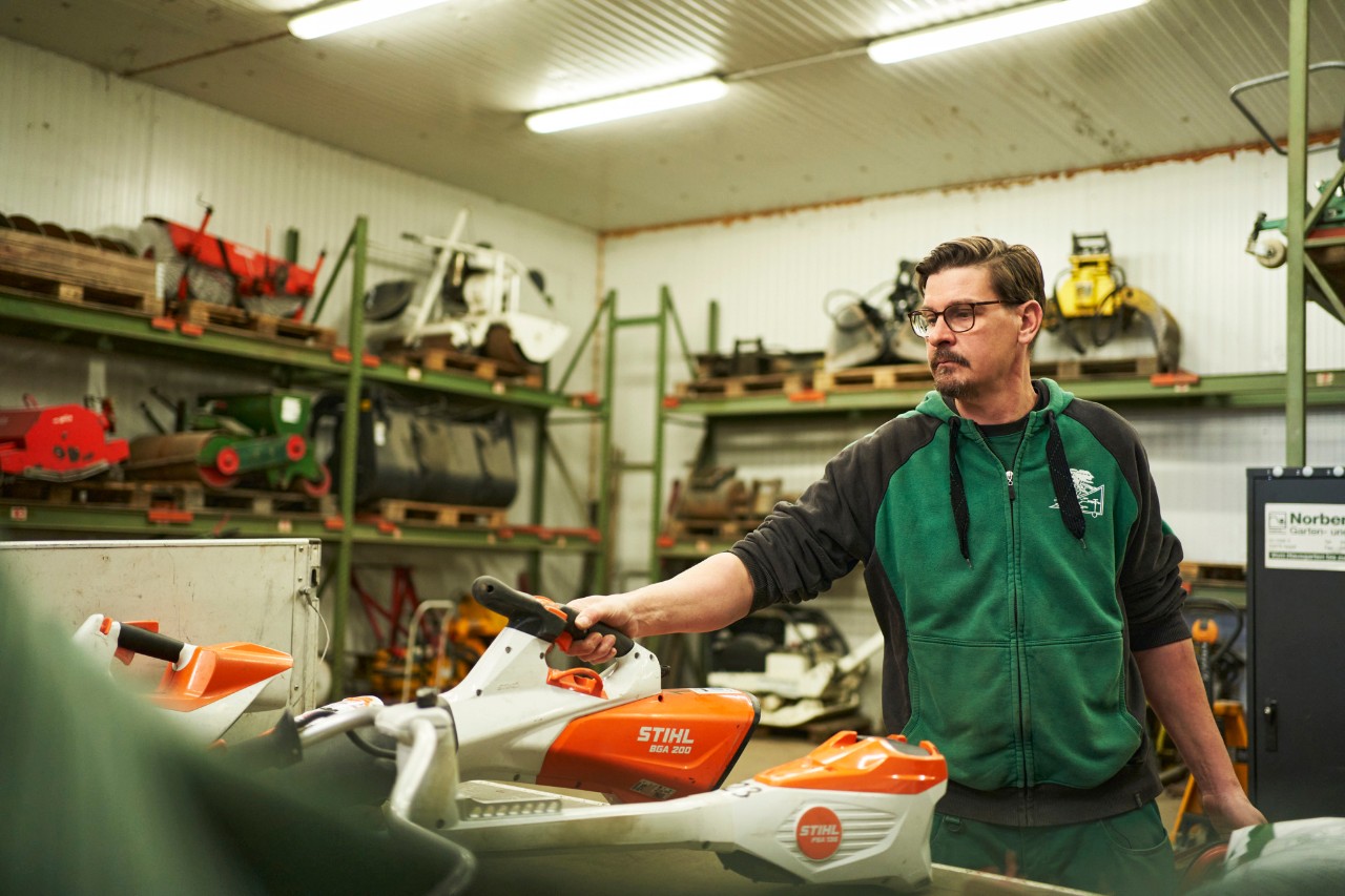 Un bărbat într-un atelier se află în spatele unei zone de lucru cu utilaje cu acumulator STIHL, apucând suflanta de frunze cu acumulator STIHL BGA 200