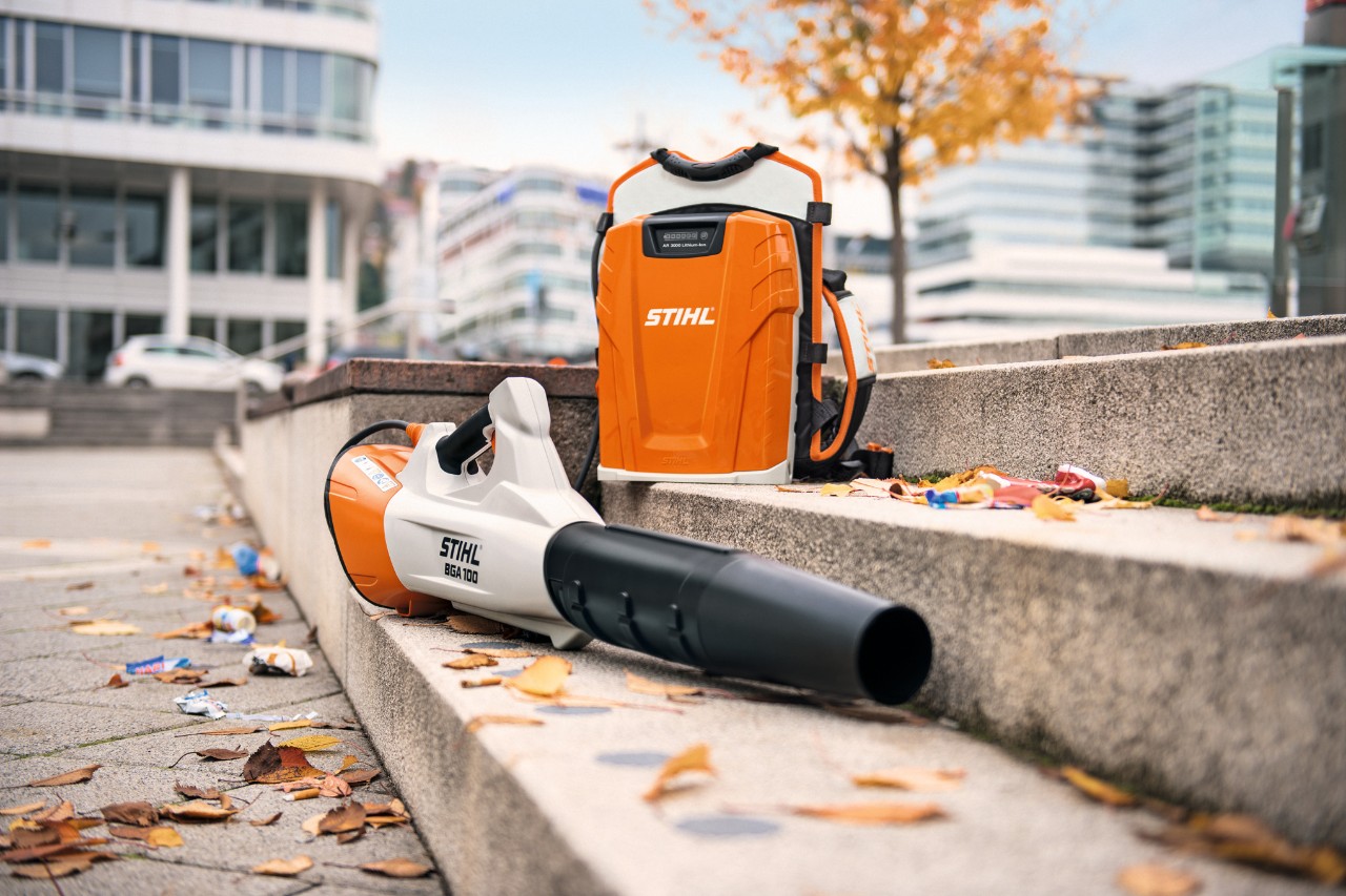 Suflanta de frunze cu acumulator STIHL BGA 100 și acumulatorul profesional care poate fi purtat pe spate STIHL AR 3000 L se află pe o scară de piatră cu câteva frunze