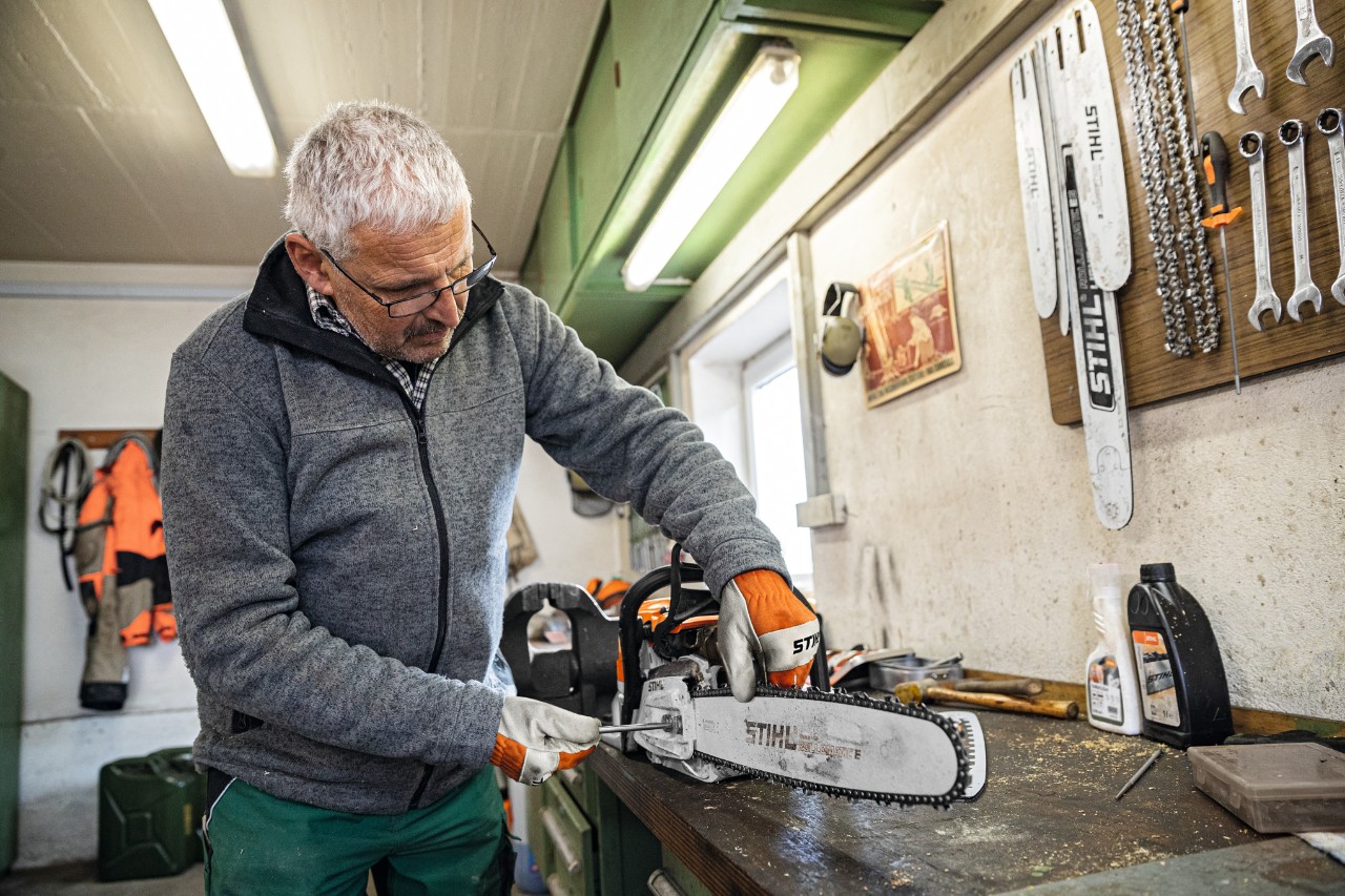 Într-un atelier un bărbat montează șina port-lanț STIHL Rollomatic E la un motoferăstrău 