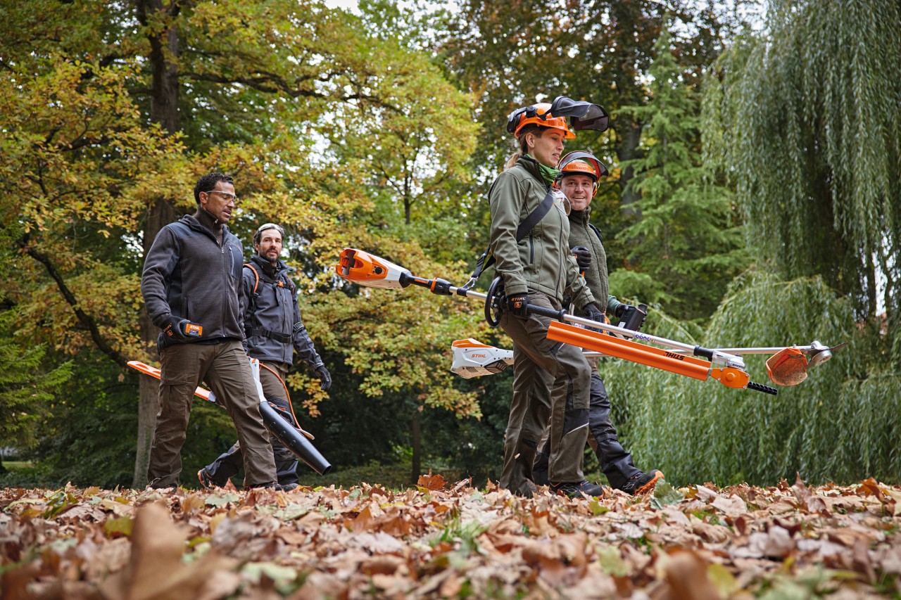 Patru profesioniști STIHL cu utilaje cu acumulator merg de-a lungul unui drum