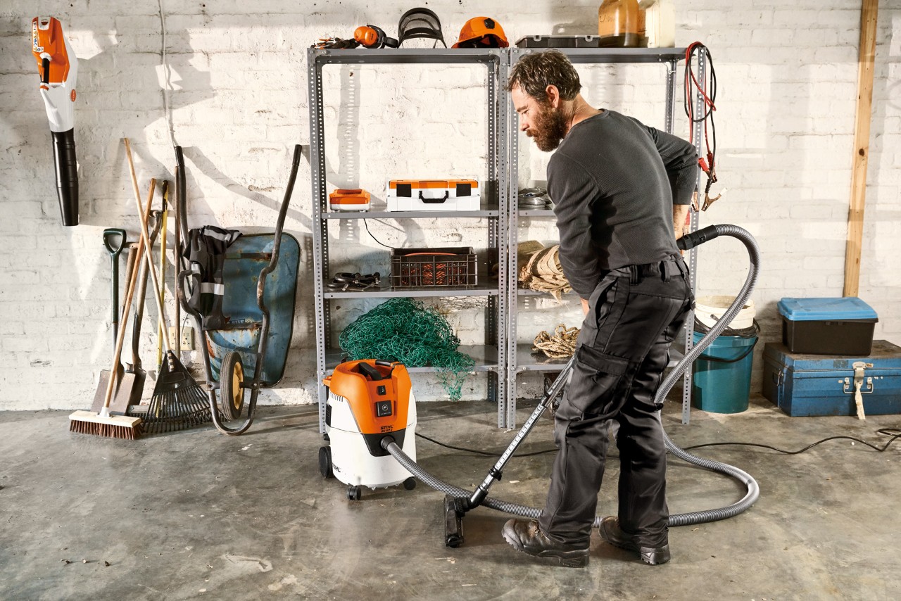 Un bărbat aspiră podeaua unui garaj cu aspiratorul pentru suprafețe umede și uscate STIHL SE 62 E