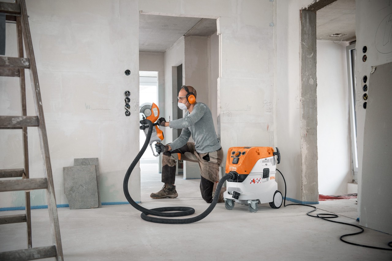 Un bărbat utilizează aspiratorul pentru suprafețe umede și uscate STIHL SE 133 ME în timp ce lucrează cu motodebitatorul STIHL TSA 230