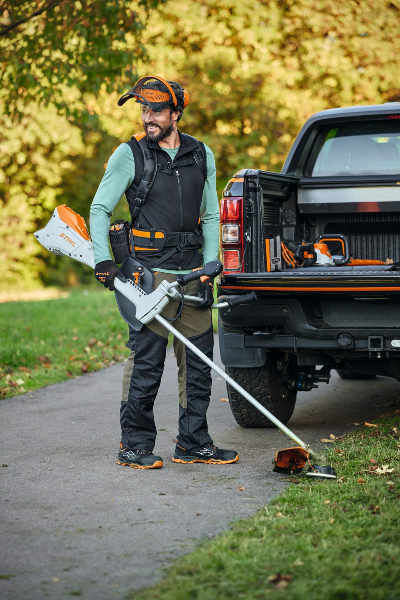 Un bărbat cu setul FS și o motocoasă cu acumulator STIHL FSA 200 în fața unei mașini