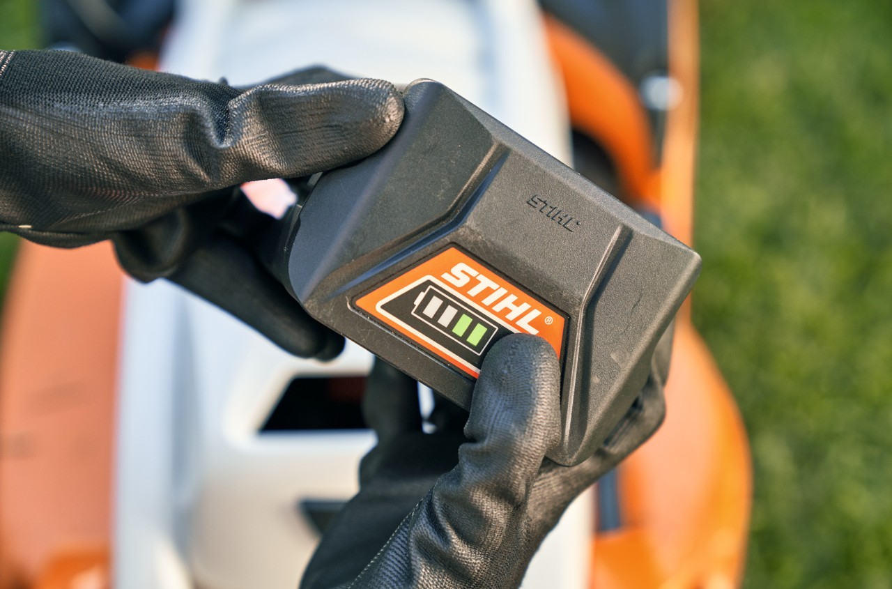 Acumulator litiu-ion STIHL, în fundal o mașină de tuns iarba cu acumulator STIHL RMA 339 C