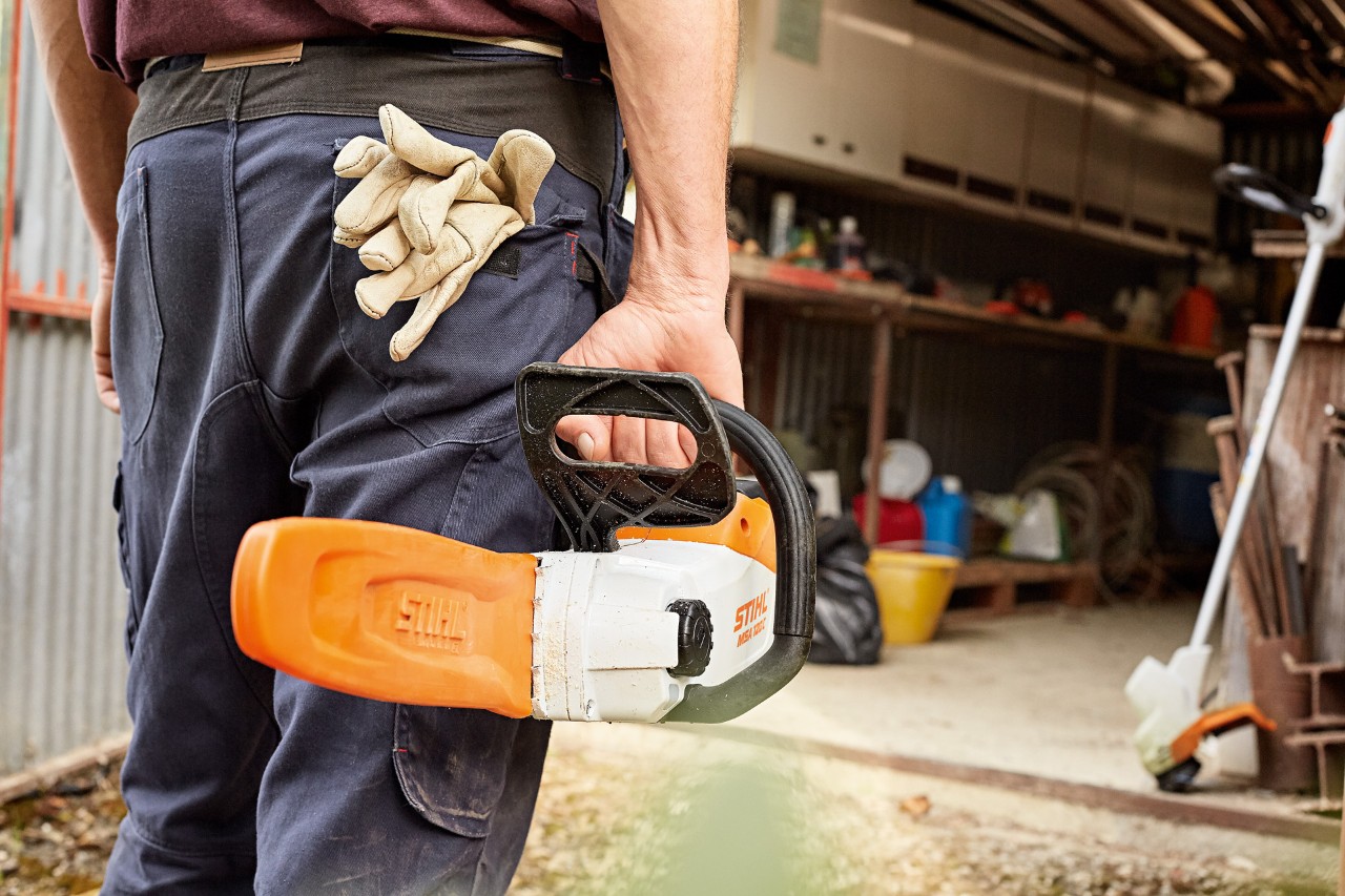 Un bărbat stă în fața atelierului cu ferăstrăul cu acumulator STIHL cu apărătoare de șină