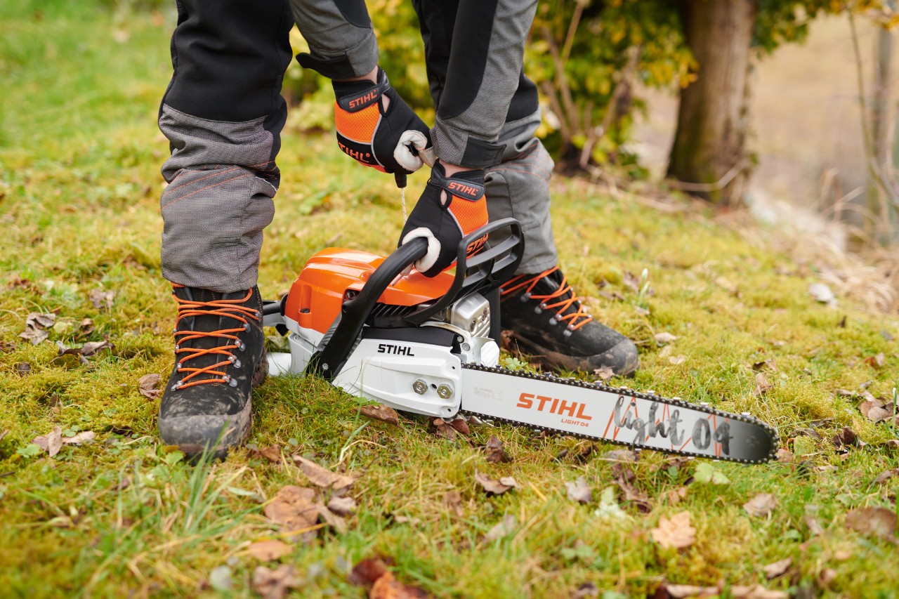 Motoferăstrăul STIHL MS 261 C-M a fost așezat pe sol în pădure pentru ca apoi să poată fi pornit în siguranță de către persoană.