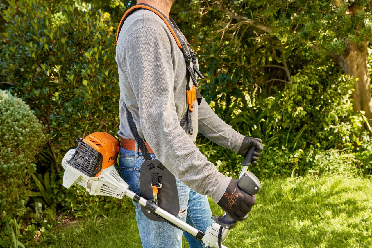 Un bărbat ridică motocoasa STIHL FS 91 de pe sol pentru a începe tunderea ierbii 