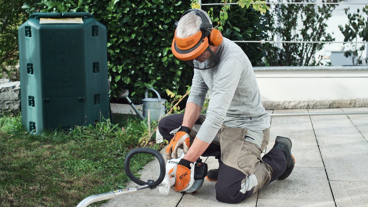Motocoasa pe benzină STIHL FS 38 este fixată pe sol de o persoană care poartă îmbrăcăminte de protecție