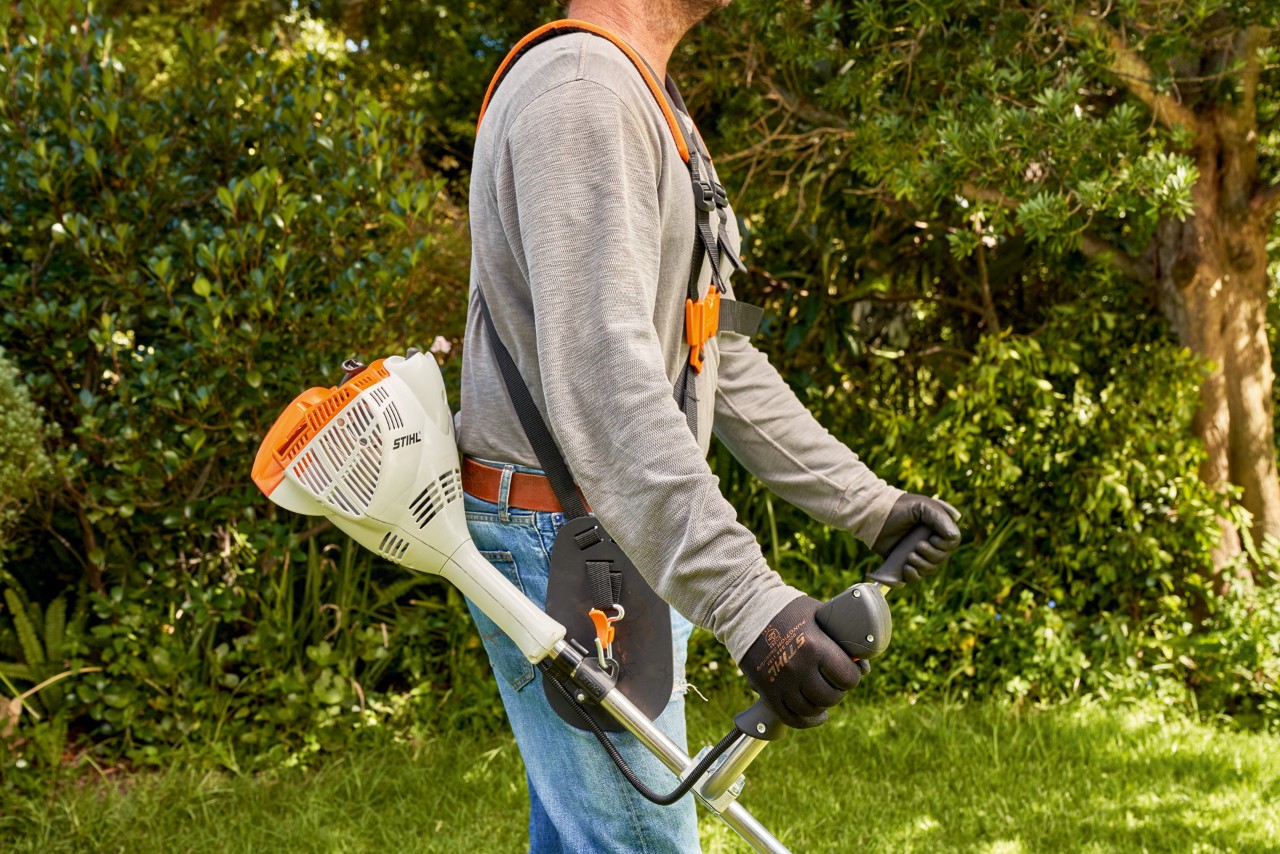 Un bărbat ridică motocoasa pe benzină STIHL FS 56 de pe sol