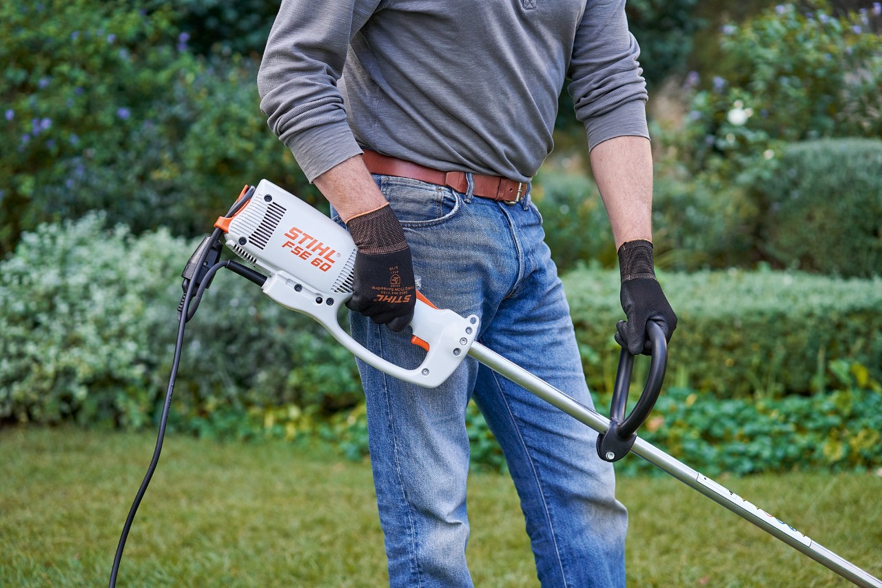 Un bărbat cu mănuși de protecție ține motocoasa electrică STIHL FSE 60 cu ambele mâini