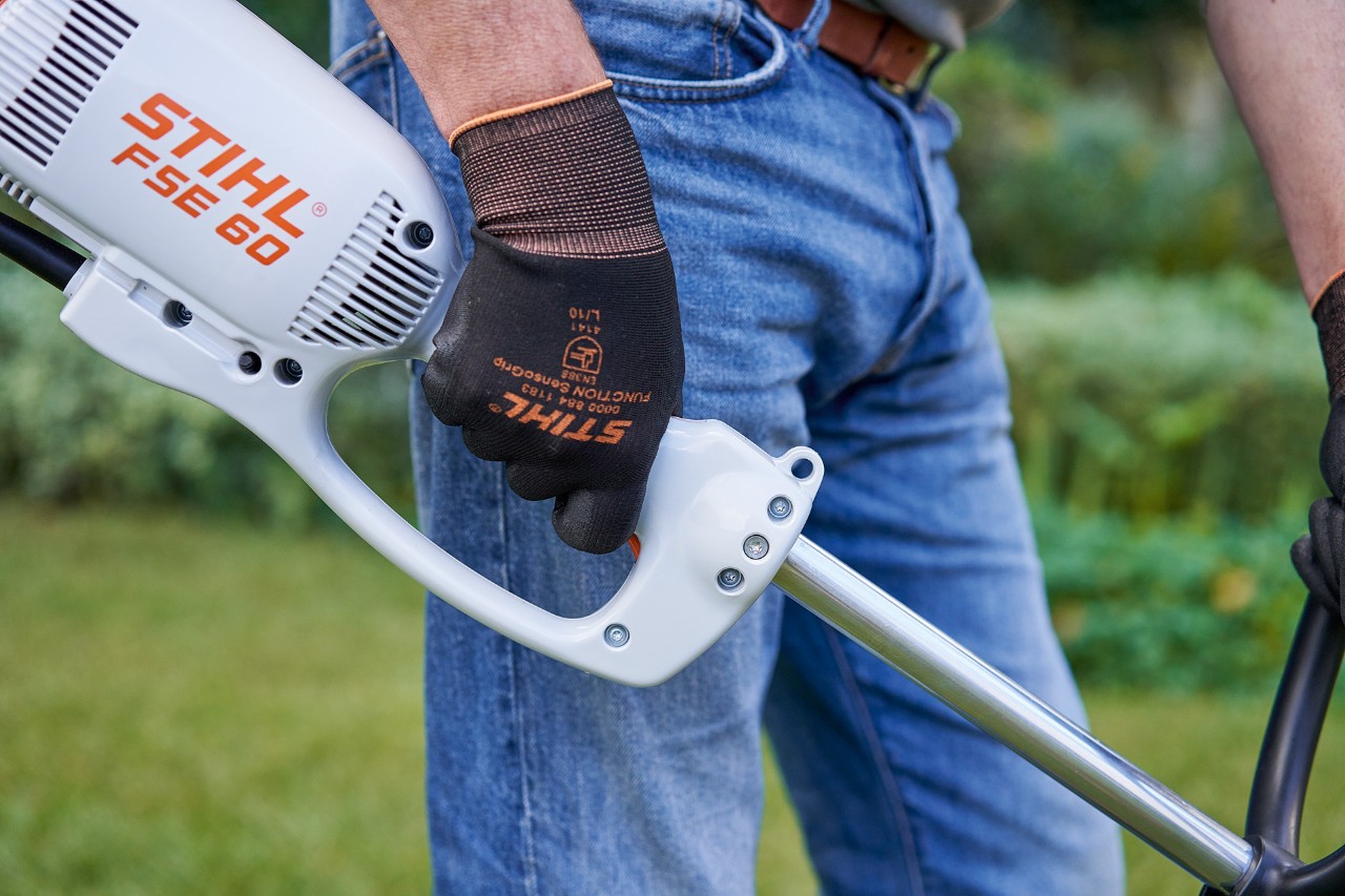 Un bărbat apasă comutatorul de pe mânerul de comandă al motocoasei electrice STIHL FSE 60