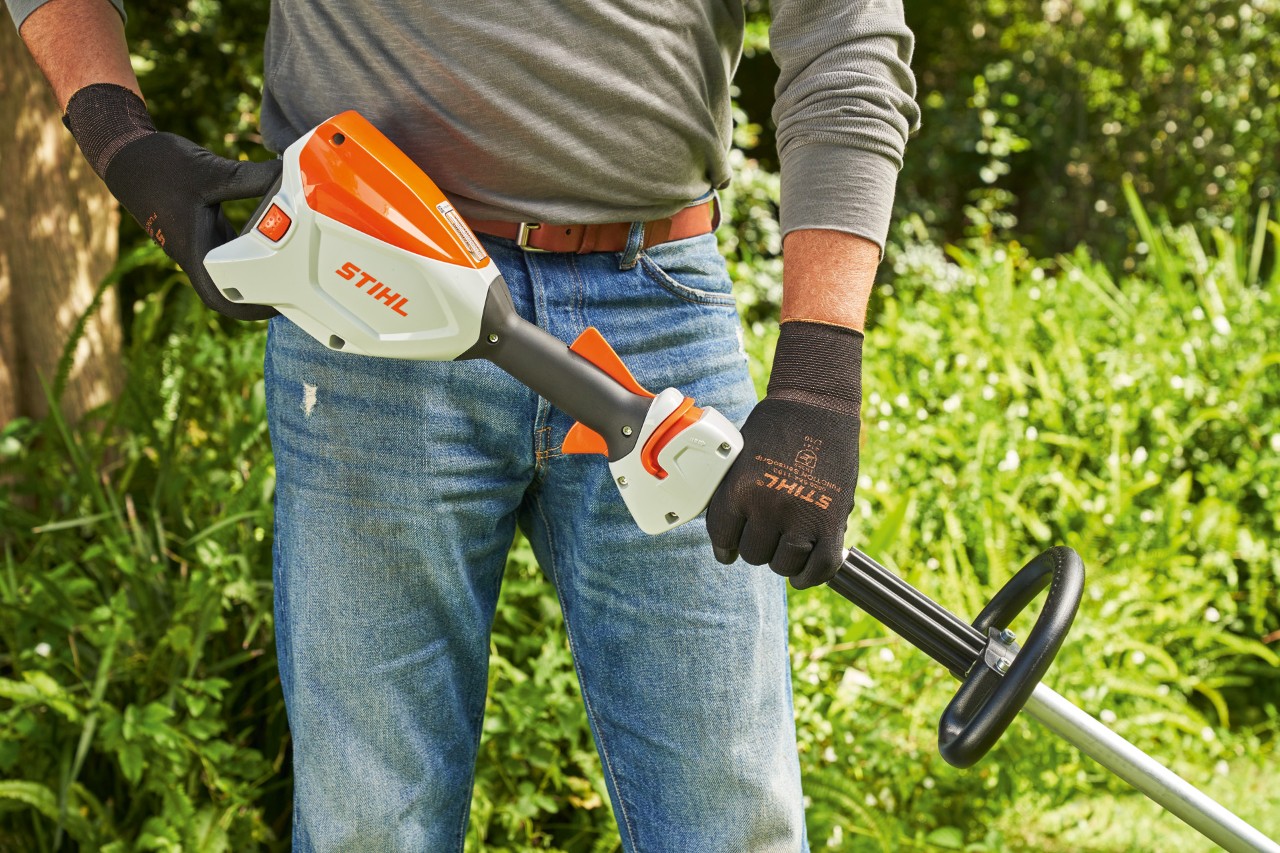 Un bărbat cu mănuși de protecție verifică acumulatorul motocoasei cu acumulator STIHL FSA 60 pentru a porni motocoasa