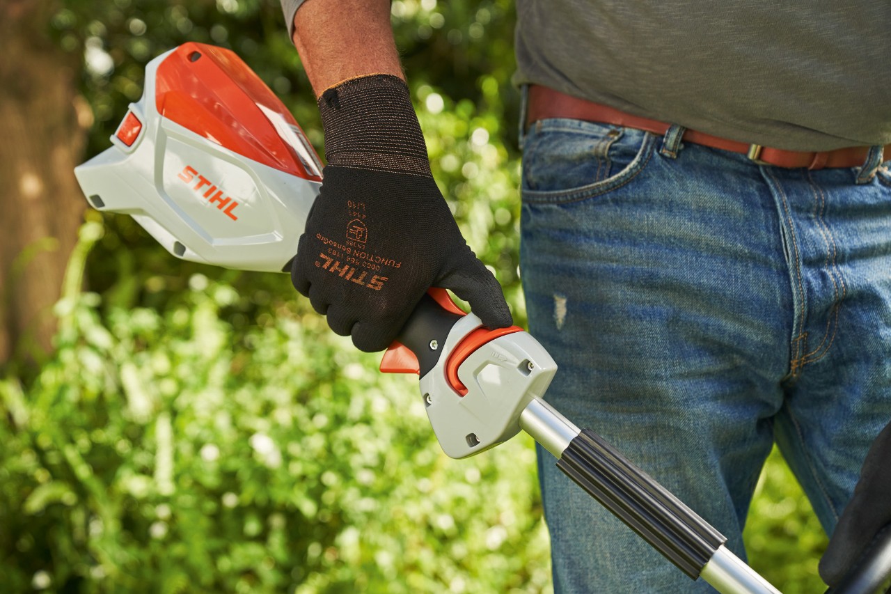 Un bărbat cu mănuși de protecție, împinge cursorul de deblocare al motocoasei cu acumulator STIHL FSA 60 spre mânerul circular