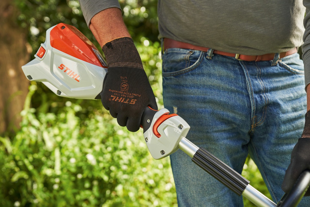 Un bărbat cu mănuși de protecție acționează maneta de acționare a motocoasei cu acumulator STIHL FSA 60 pentru a o porni