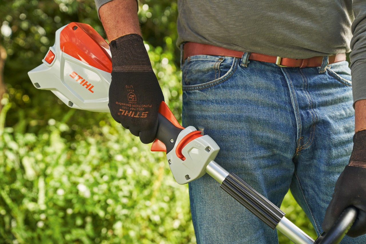 Un bărbat cu mănuși de protecție eliberează maneta de acționare a motocoasei cu acumulator STIHL FSA 60 pentru a o opri