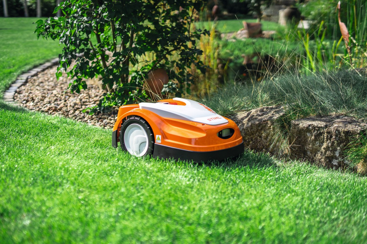 STIHL iMOW RMI 422 tunde iarba pe o pajiște în grădină, la marginea unui mic zid de piatră.