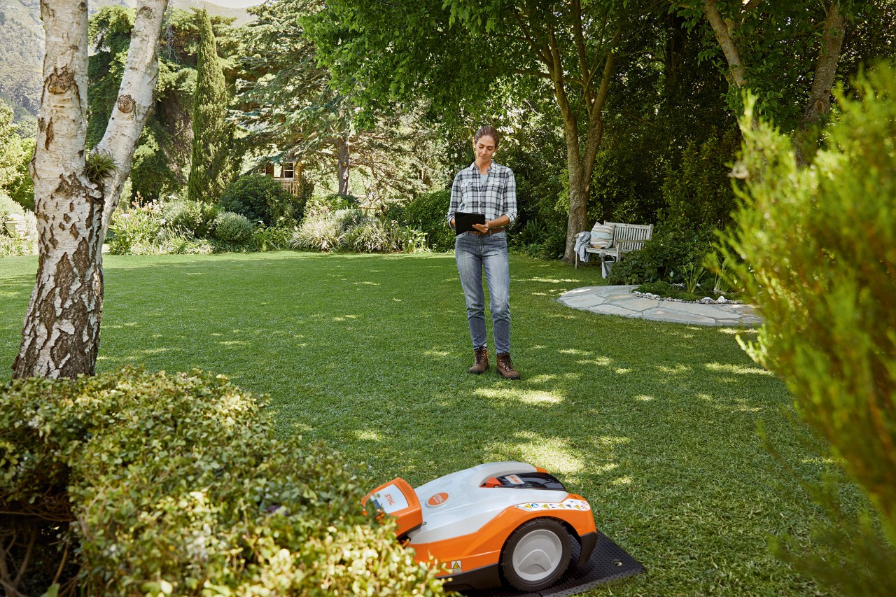 O femeie operează robotul de tuns iarba STIHL iMOW® 522 prin intermediul unei tablete