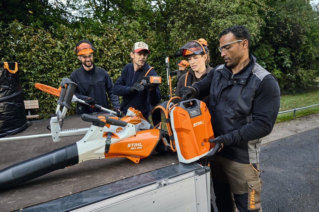 O echipă de profesioniști în amenajarea peisajului descarcă echipamentele profesionale STIHL alimentate cu baterie din zona de încărcare a unui vehicul.