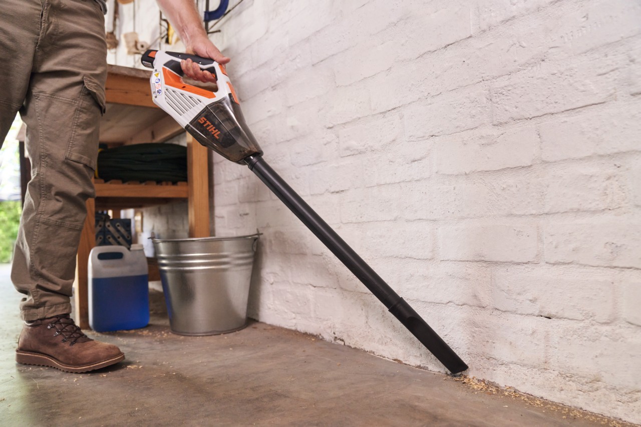 Prim-plan al unei persoane care aspiră podeaua unui atelier cu un aspirator de mână cu acumulator STIHL SEA 20 