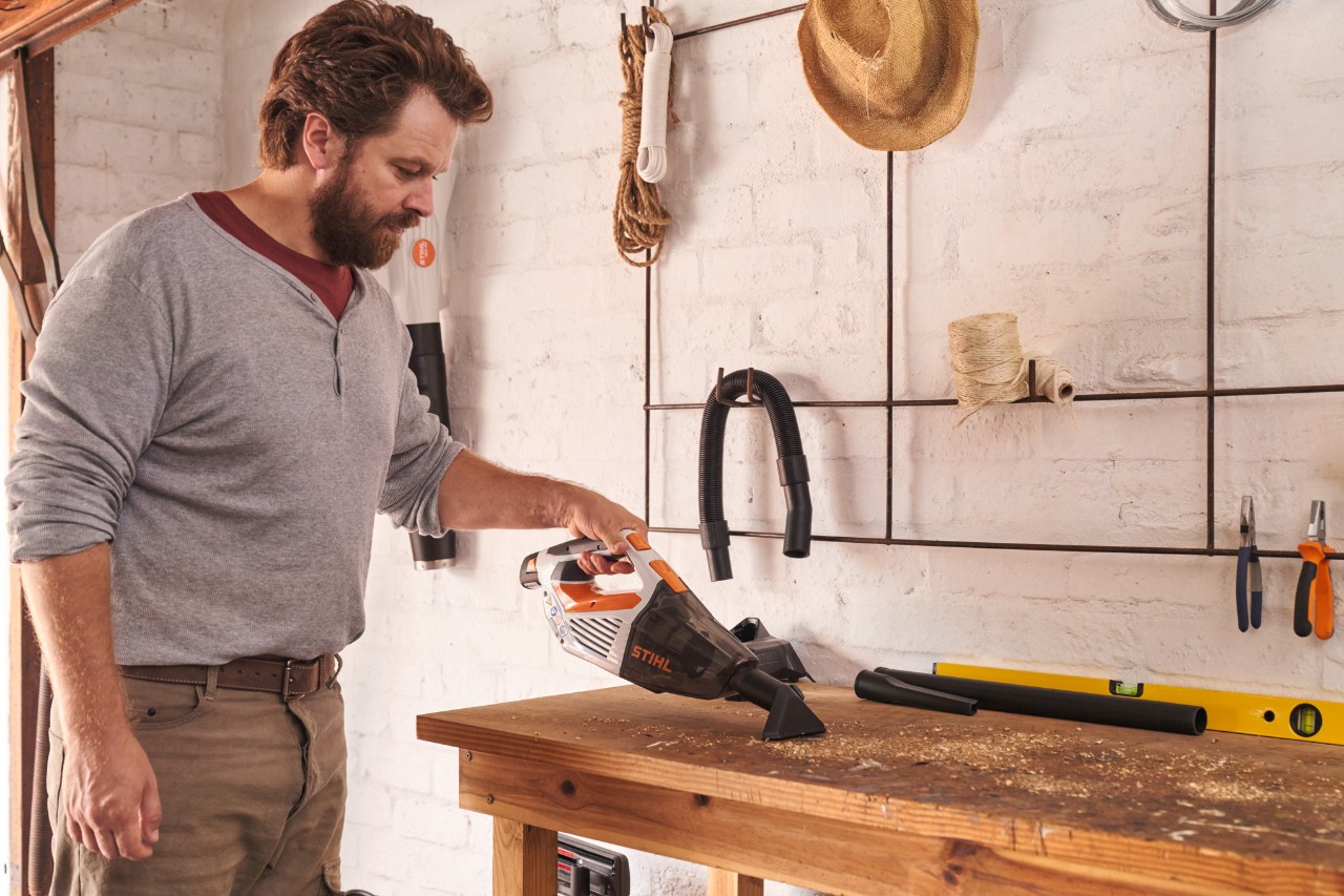 Un bărbat aspiră un banc de lucru cu un aspirator de mână cu acumulator STIHL SEA 20