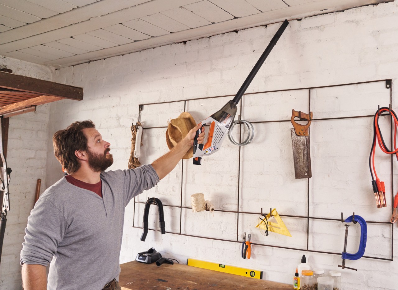 Un bărbat curăță tavanul unui atelier cu un aspirator de mână cu acumulator STIHL